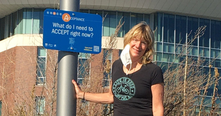 Senior Lecturer in Nursing Linda Chiofar stands by a sign on the Grace Trail